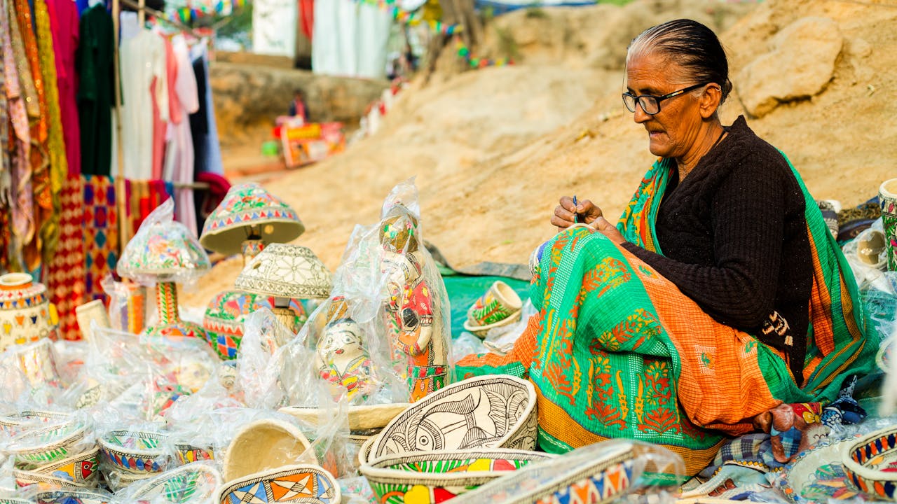 A woman hand-paints traditional crafts at an outdoor market, showcasing vibrant ethnic designs.