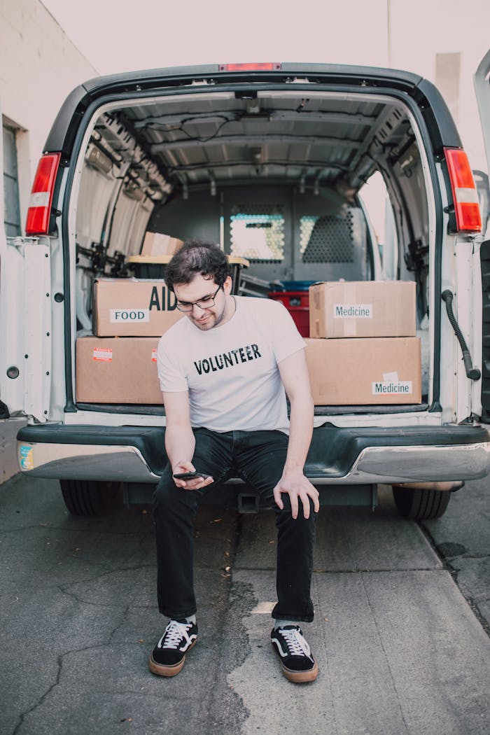 A volunteer organizing food and medicine boxes in a delivery van, preparing for charity distribution.