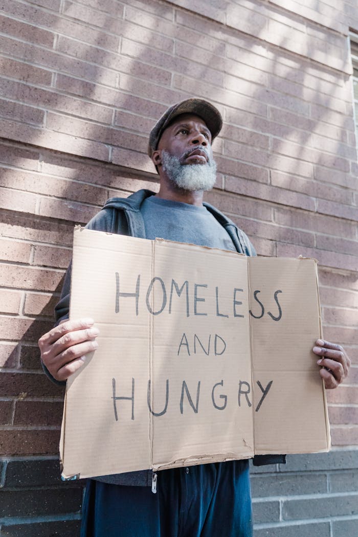 African American man standing outdoors holding 'Homeless and Hungry' sign.